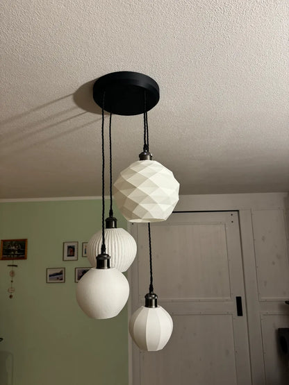 A modern multi-light pendant ceiling fixture with three white faceted and ribbed glass globes hanging from a black ceiling canopy in a home interior.