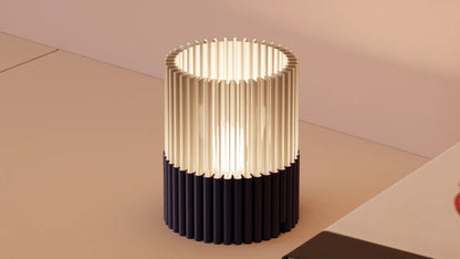 Modern cylindrical table lamp with black and gold design on a beige surface.