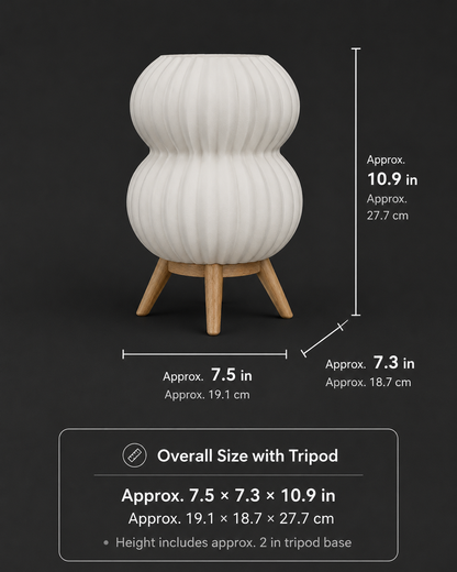 A white ribbed vase-shaped planter with a wooden tripod base on a dark background, with overlaid dimension lines and text showing approximate height, width, and base width in inches and centimeters.