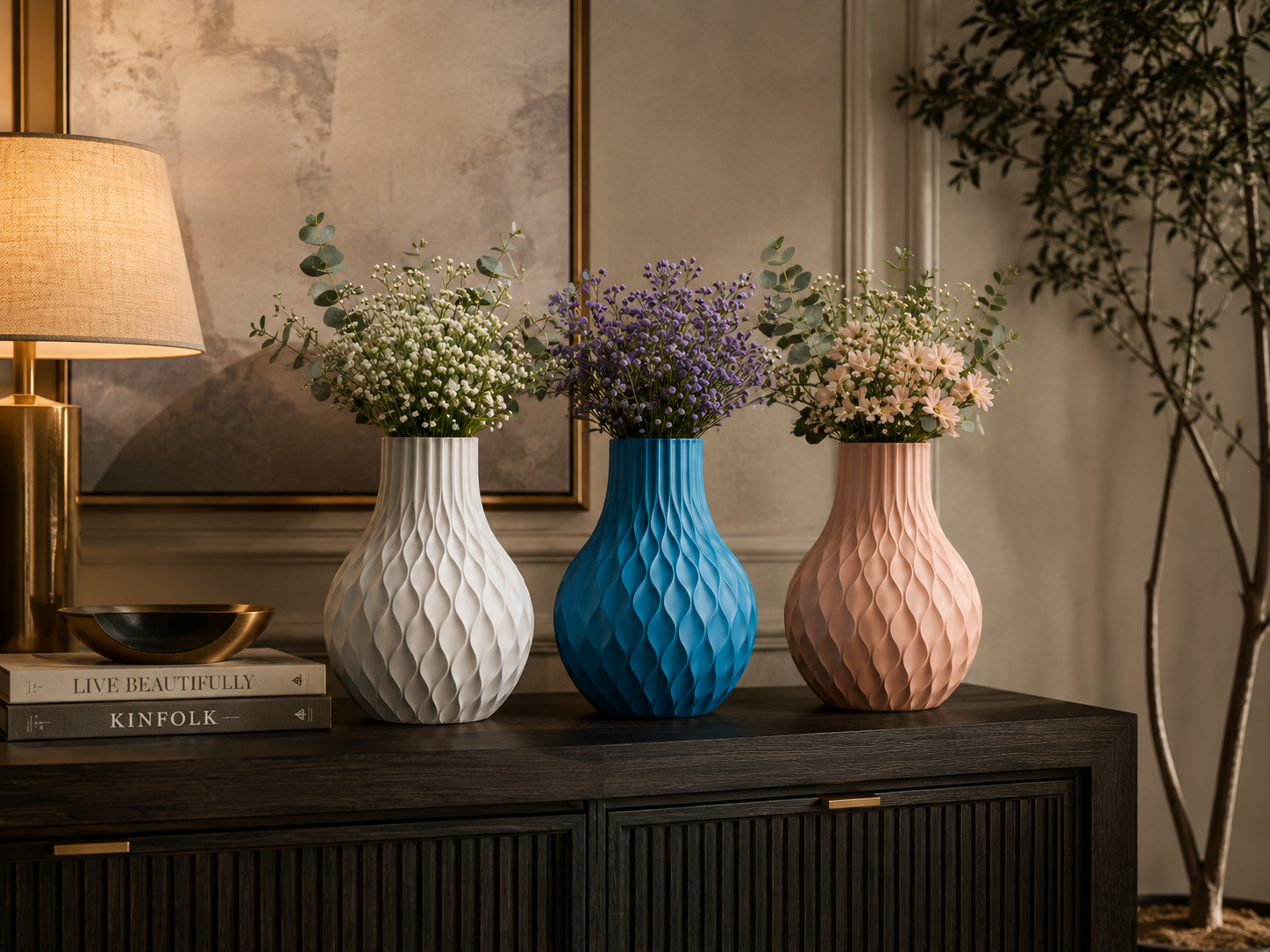 Three textured ceramic flower vases in white, bright blue, and dusty pink, filled with delicate flowers, arranged on a dark wooden console table in a warmly lit interior setting.