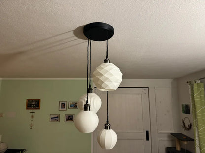 Three white faceted pendant light globes hanging from a black ceiling canopy in a home interior with a green wall and white door in the background.
