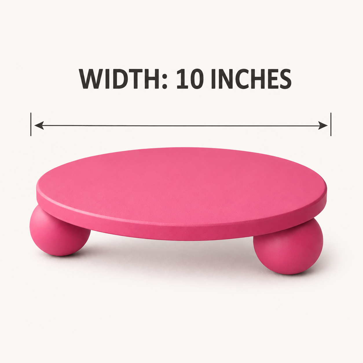 A pink round platform stool with three ball legs on a light beige background, with a dimension line and text reading 'WIDTH: 10 INCHES' above it.