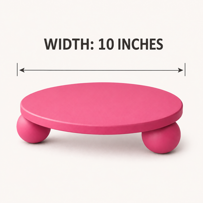 A pink round platform stool with three ball legs on a light beige background, with a dimension line and text reading 'WIDTH: 10 INCHES' above it.