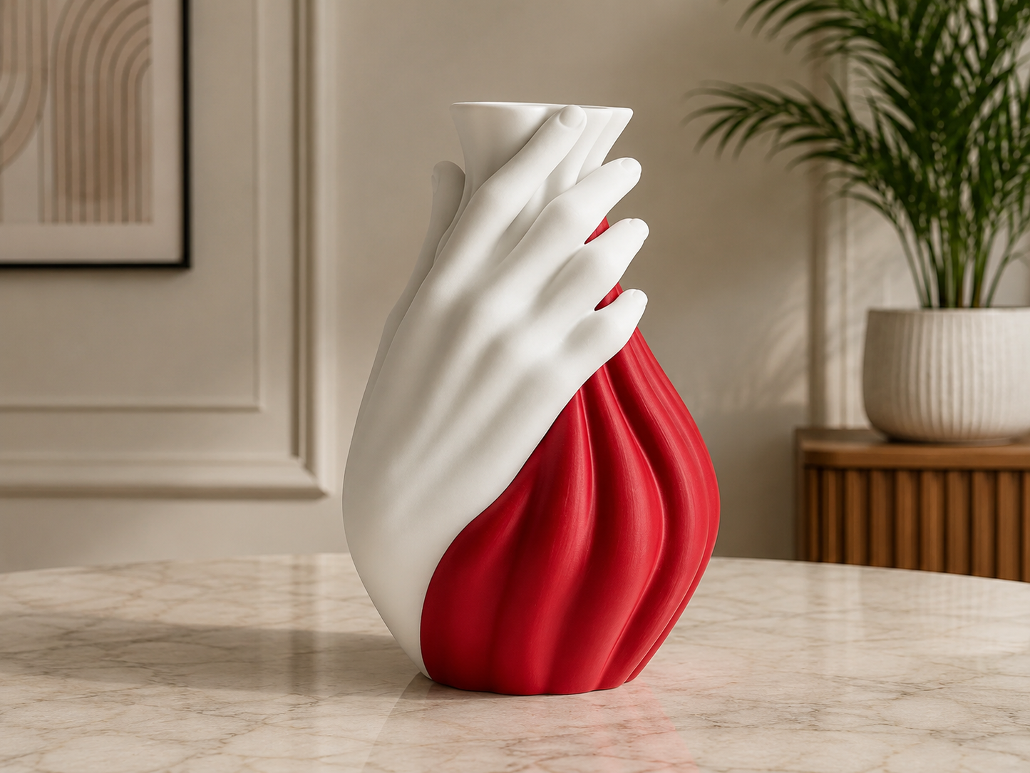 A sculptural ceramic vase shaped like a hand, with a glossy white upper portion and a deep red lower body, displayed on a light marble tabletop in a modern interior setting.