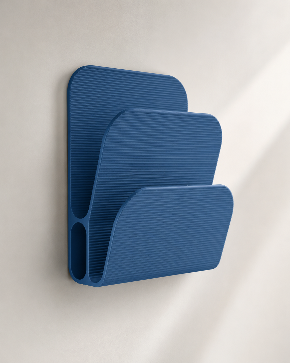 A three-tier blue wall-mounted bookshelf with a ribbed, modern design, shown against a neutral off-white wall with soft diagonal shadows.