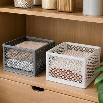 Two square plastic mesh storage baskets in gray and white, shown on a wooden shelf with folded textiles inside. The baskets have a lattice open design and are displayed in a home interior setting.