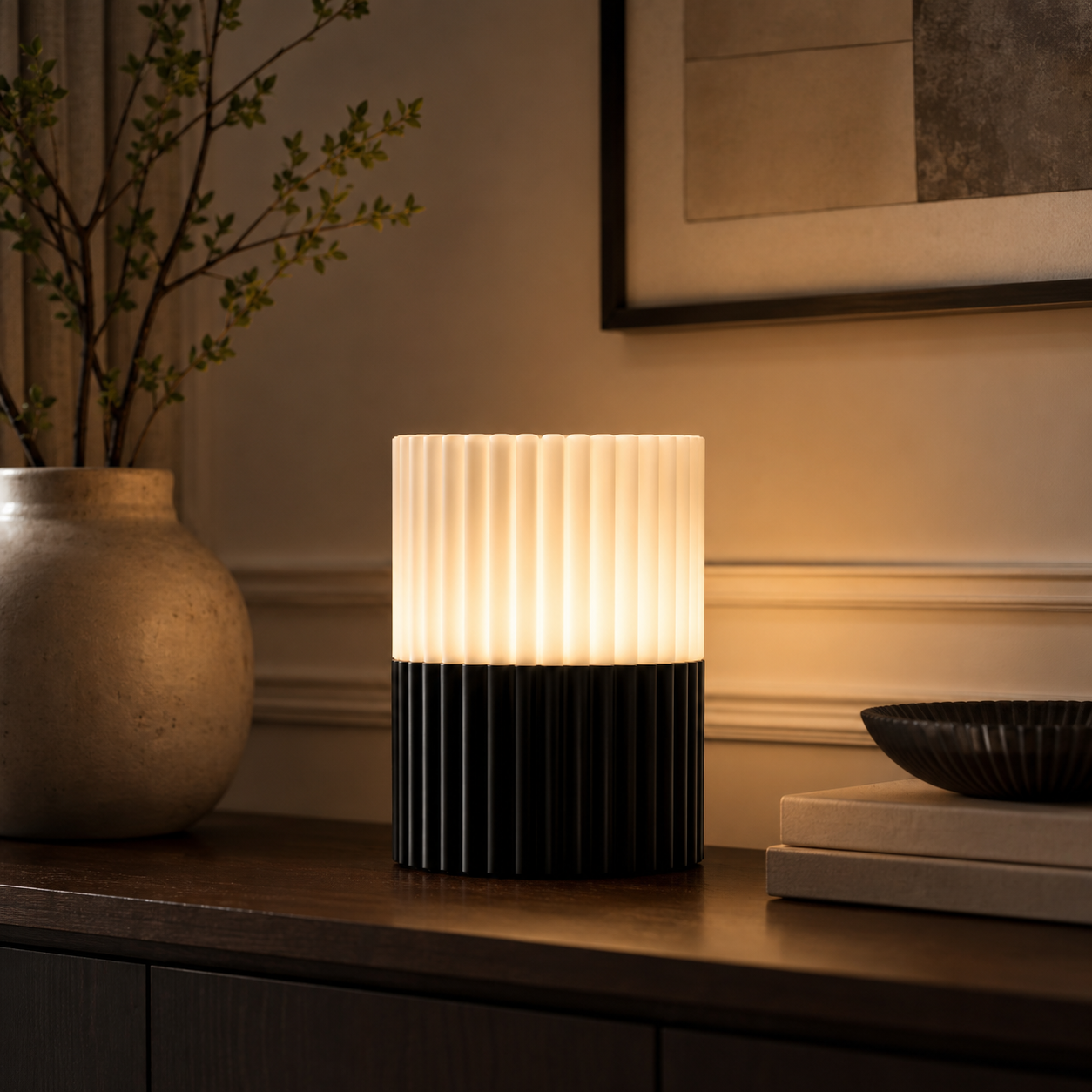 A modern table lamp with a ribbed cylindrical design, featuring a glowing warm white upper section and a matte black lower section, styled on a dark wooden console table in a warm, elegant interior setting.
