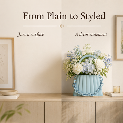 A styled interior scene with a light blue ribbed flower basket vase holding a bouquet of white and pale blue flowers, placed on a wooden cabinet against a cream wall. Framed art and a candle are visible in the background, with decorative text above reading 'From Plain to Styled' and smaller phrases 'Just a surface' and 'A décor statement'.