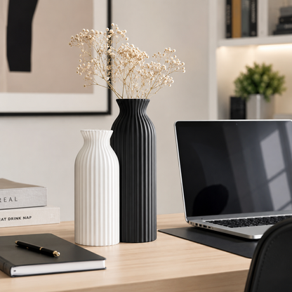 Two ribbed ceramic vases, one white and one black, with dried baby's breath stems, styled on a wooden desk next to a laptop in a modern home office setting.