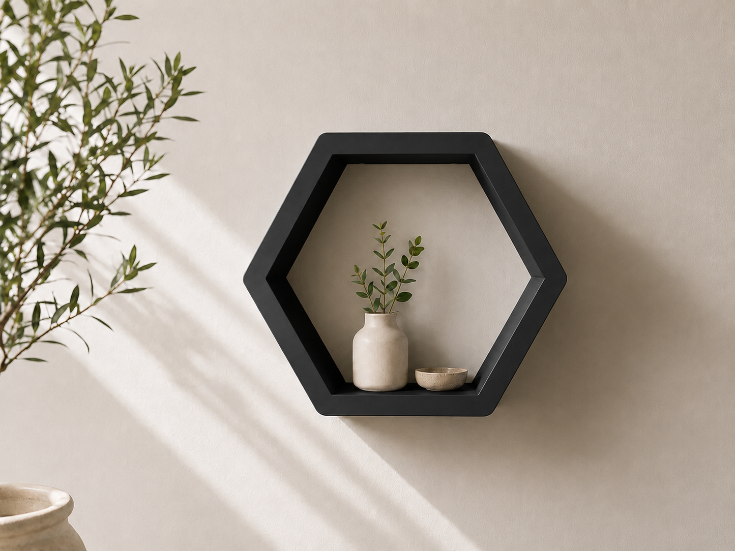 A hexagonal black floating wall shelf mounted on a beige wall, styled with a small white ceramic vase holding a green sprig and a small dish.